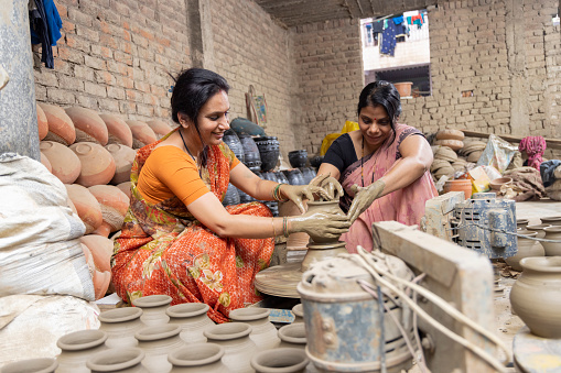 Two Indian women potters making finishing touches to the clay pot on pottery wheel.